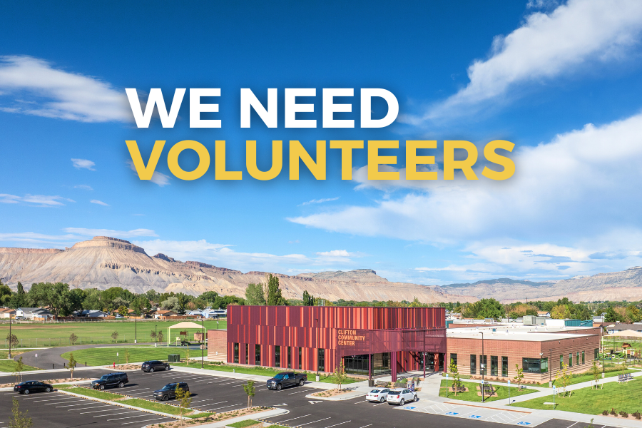 Red Clifton Community Center building with white and yellow text reading “we need volunteers.” Mount Garfield and the Book Cliffs are in the background of the picture.